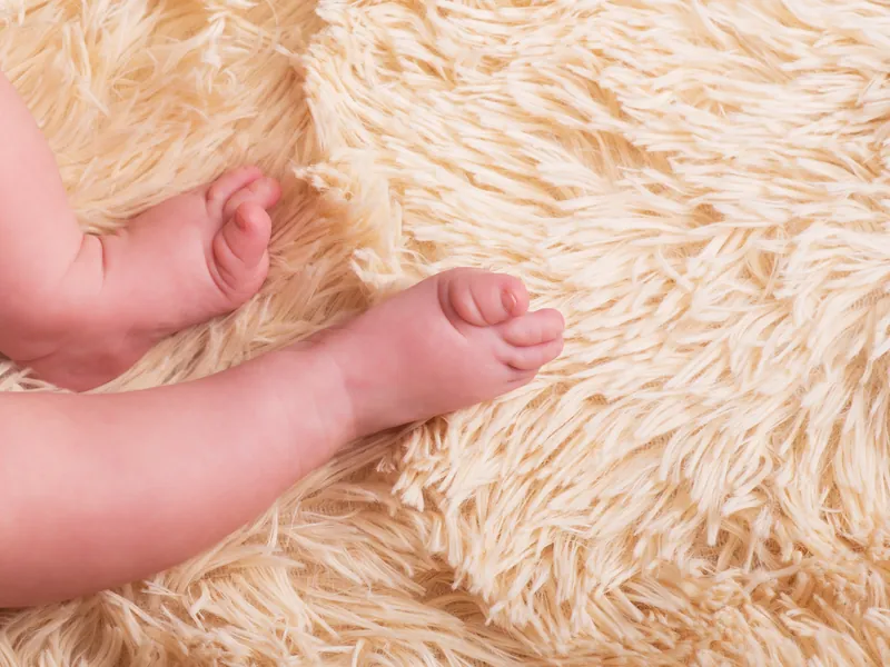 Füße eines Säuglings auf einer cremefarbenen Kuscheldecke in warmem Tageslicht