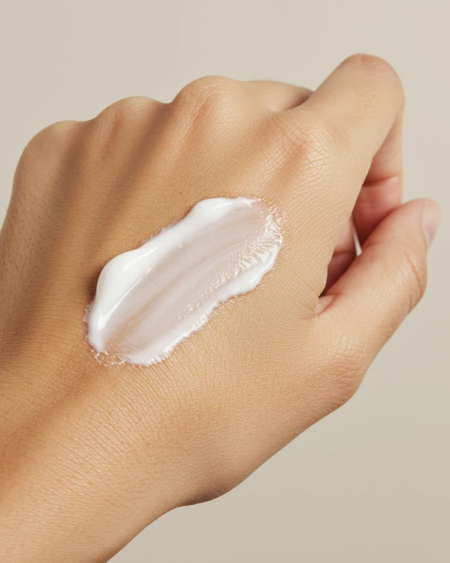 Ein Strich weiße Pflegecreme auf dem Handrücken vor einem warm beigen Hintergrund