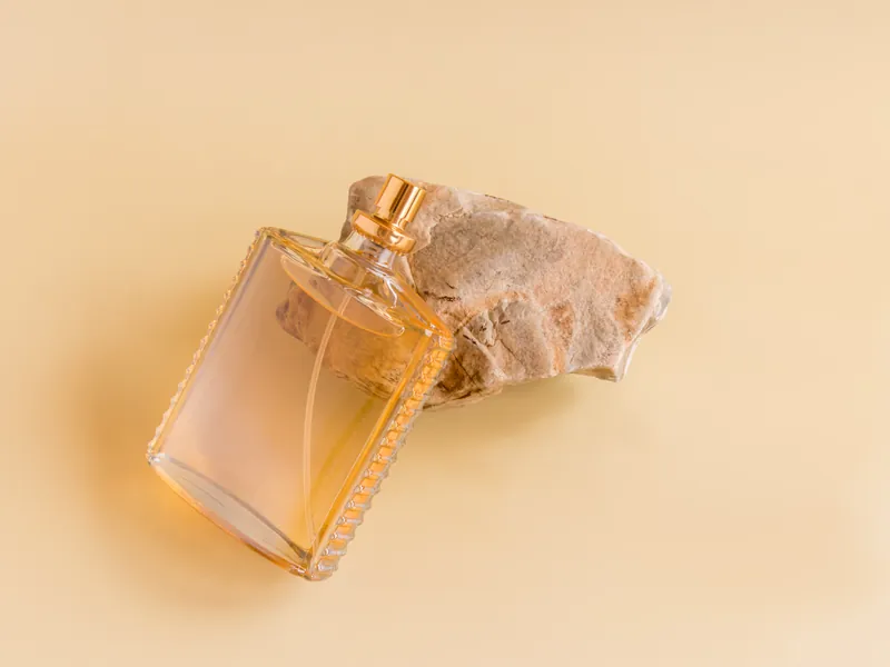 Glasflakon Parfum ohne Etikett mit goldenem Verschluss auf beigem Untergrund