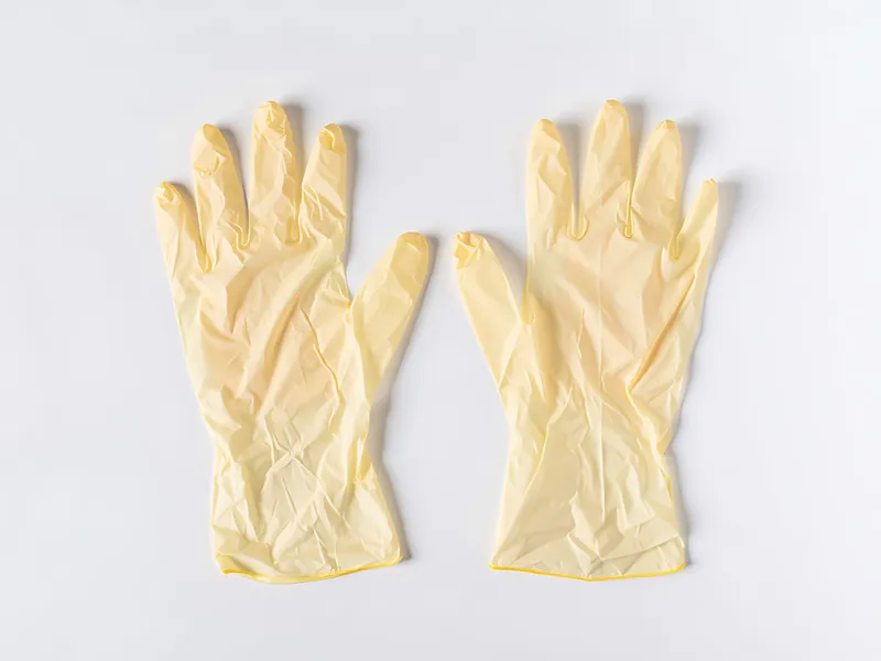 Paar cremefarbene Latexhandschuhe nebeneinander auf hellem Untergrund
