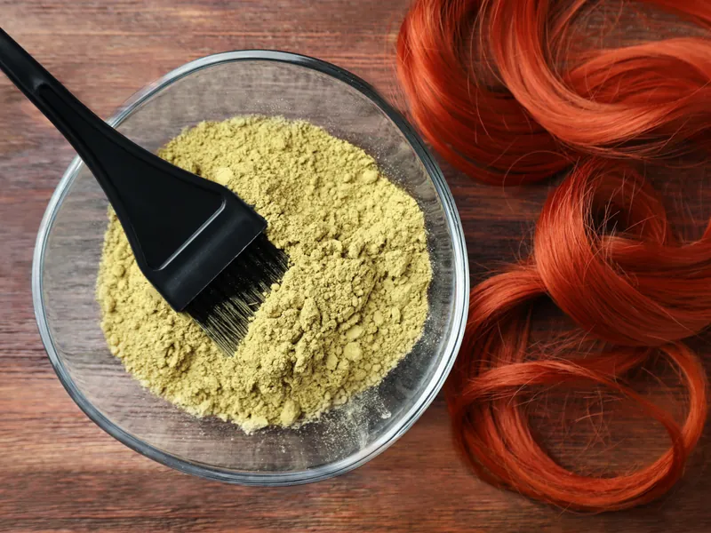 Glasschale mit Henna-Pulver, Färbepinsel und rote Haarsträhne auf Holztisch