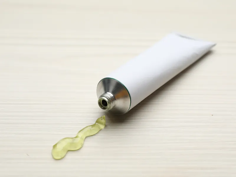 Geöffnete weiße Salbentube ohne Beschriftung mit Salbenklecks auf hellem Holztisch