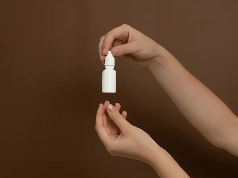 Hand hält ein kleines Tropffläschchen über die geöffnete Handfläche